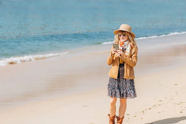 海滩上拿着手机散步的女人 — 图库照片