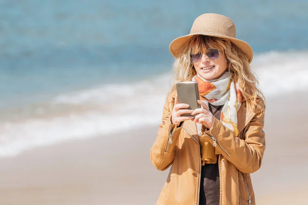 海滩上拿着手机散步的女人 — 图库照片