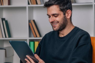 Genç adam evde dijital tablet veya dizüstü bilgisayarla çalışıyor