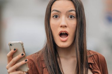 portrait of surprised girl with mobile phone outdoors