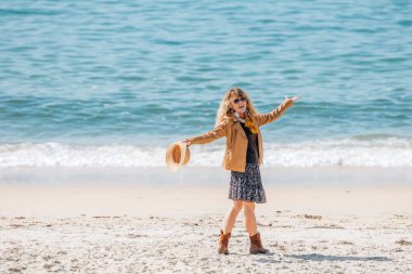 Orta yaşlı giyinmiş bir kadın sahilde eğleniyor.