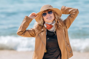 Orta yaşlı giyinmiş bir kadın sahilde eğleniyor.