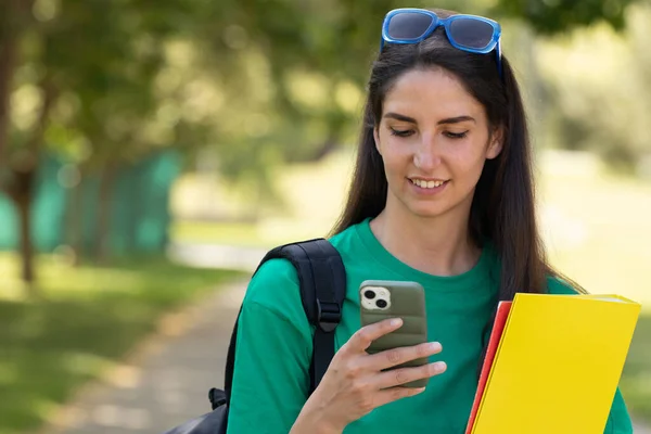 student with mobile phone and books outdoors