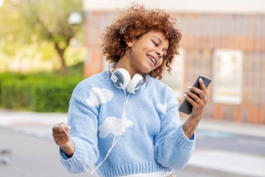 Dışarıda cep telefonuna bakan Afro-Amerikan kadın.