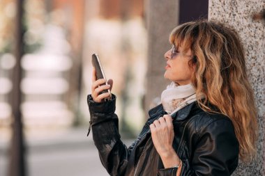 Alışveriş caddesinde çantalı ve cep telefonlu bir kadın.