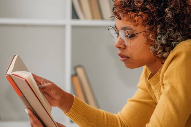 Kız evde rahatça ders kitabı okuyor.