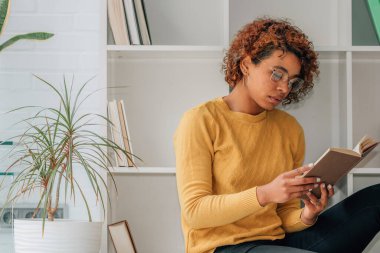 Kız evde rahatça ders kitabı okuyor.