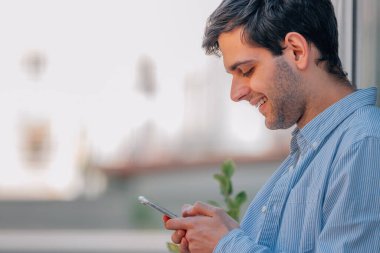 Genç adam sokakta cep telefonuna bakıyor.