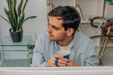 Bilgisayarın önünde bir fincan kahveyle düşünceli bir adam.