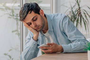 young man at home bored looking at mobile phone