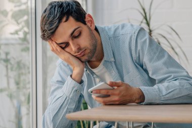 young man at home bored looking at mobile phone