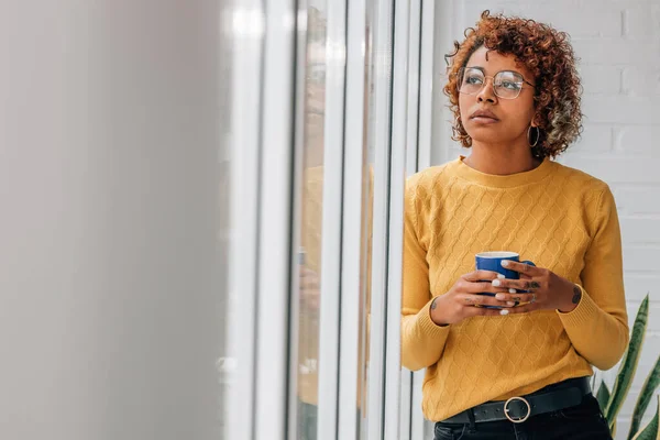 african american woman or girl with cup of coffee at home looking out the window