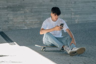 Cep telefonu ve kaykayı olan genç bir adam.