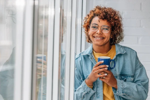 african american woman smiling at window with cup of coffee