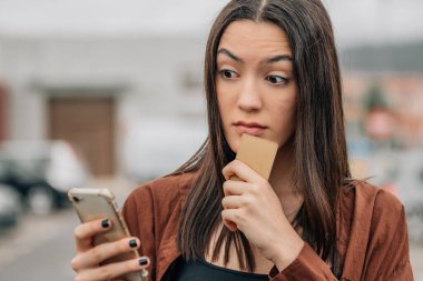 Şaşırmış kredi kartı ve cep telefonu alan ya da internetten ödeme yapan bir kız.