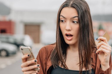 Şaşırmış kredi kartı ve cep telefonu alan ya da internetten ödeme yapan bir kız.