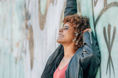 Afro-Amerikalı kız sokak duvarında mutlu bir şekilde gülümsüyor.