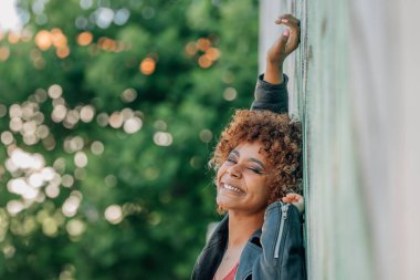 Afro-Amerikalı kız sokak duvarında mutlu bir şekilde gülümsüyor.