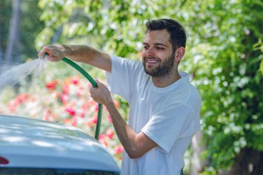 Yazın genç adam arabayı hortumla yıkıyor.