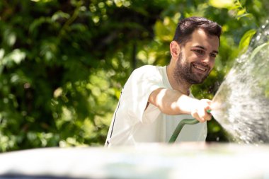 Yazın genç adam arabayı hortumla yıkıyor.