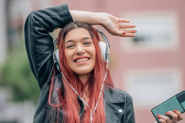 Kızıl saçlı kız mutlu gülümsüyor, cep telefonu ve kulaklıkla sokakta.