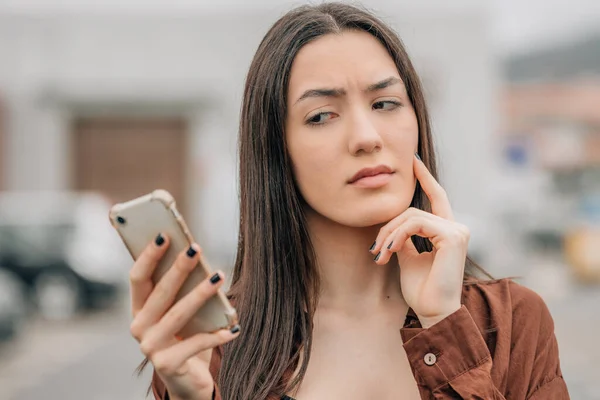 Menina Olhando Para Telefone Celular Pensativo Com Desconfiança — Fotografia de Stock
