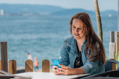 Yaz terasında cep telefonuyla oturan bir kadın.