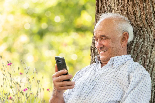 Старший Чоловік Дивиться Мобільний Телефон Або Смартфон Посміхаючись Відкритому Повітрі — стокове фото