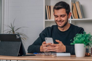 Evde cep telefonu ve dizüstü bilgisayarı olan genç adam.