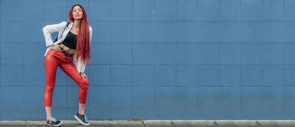 红头发 时髦的都市嬉皮士女孩躺在街道上 被蓝色的墙隔开 — 图库照片