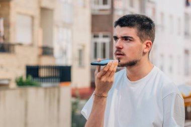 Sokaktaki genç adam cep telefonuyla sesli mesaj yolluyor.