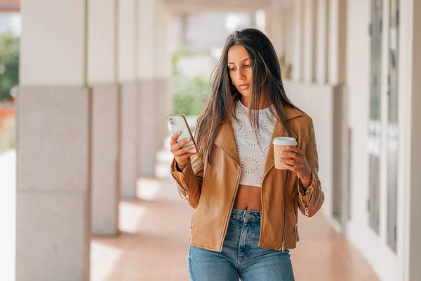 latin american girl walking with mobile phone and cup of coffee