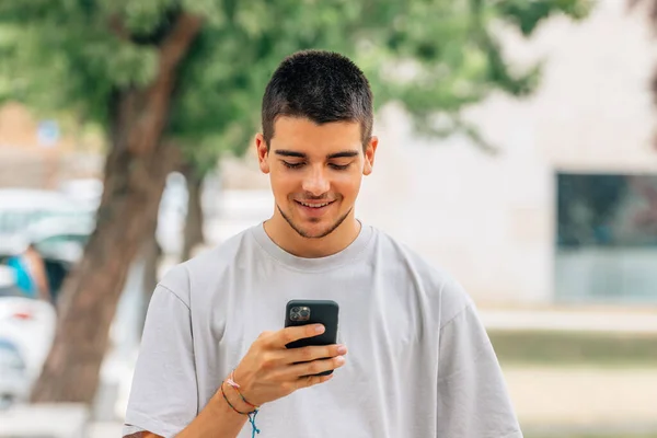Uśmiechnięty Młody Człowiek Ulicy Patrząc Telefon Komórkowy Lub Smartfon — Zdjęcie stockowe