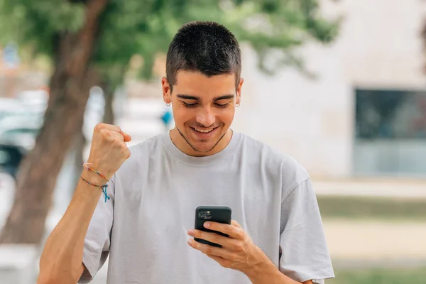 Młody Człowiek Podekscytowany Radością Patrząc Telefon Komórkowy — Zdjęcie stockowe