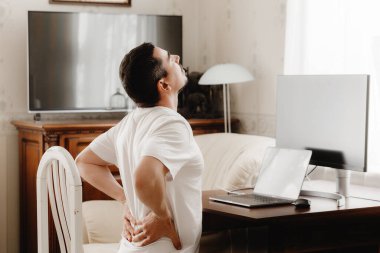 Sırtı ağrıyan bir bilgisayarla masadaki adam.