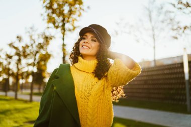 Kafasının arkasındaki el kıllarına dokunarak neşeli bir şekilde çenesini kaldırarak uzaklığa bakıyor.