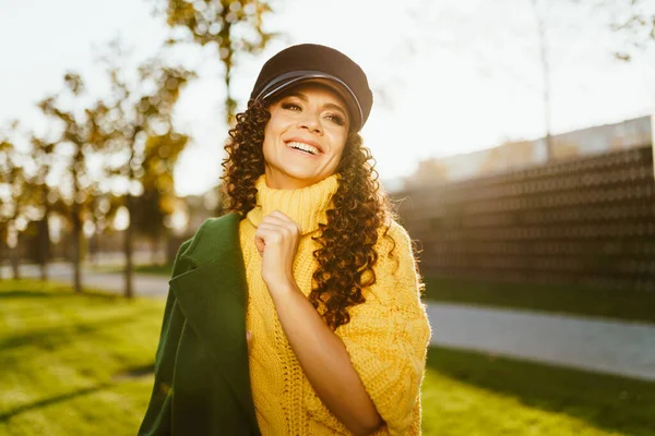 En el parque en la hierba verde se encuentra una hermosa chica en un suéter brillante y la tapa sobre el abrigo del hombro — Foto de Stock