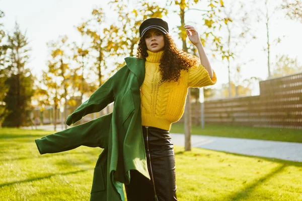 Omzundan düşen yeşil ceketli kız elini çimlerin üzerinde sallıyor.