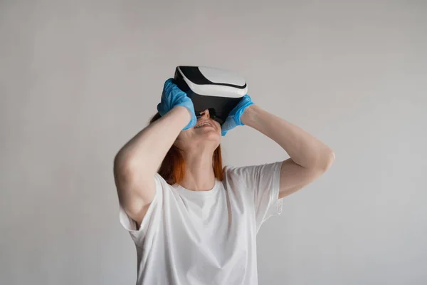 A woman in braces and a white T-shirt looks into virtual reality glasses on a white background, on hand medical gloves