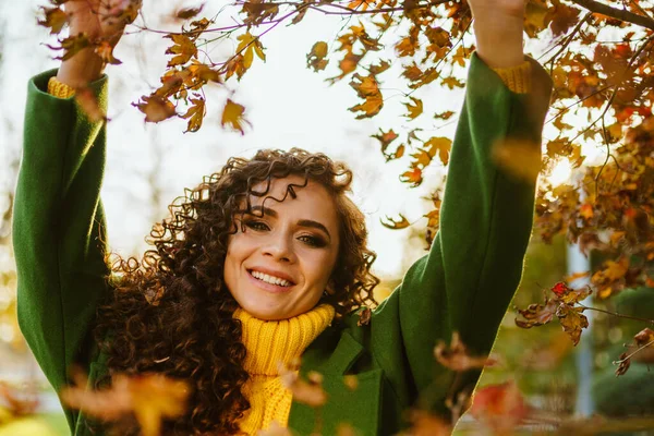 Toca sus manos hojas amarillas de otoño sobre su cabeza morena rizada con ojos verdes — Foto de Stock