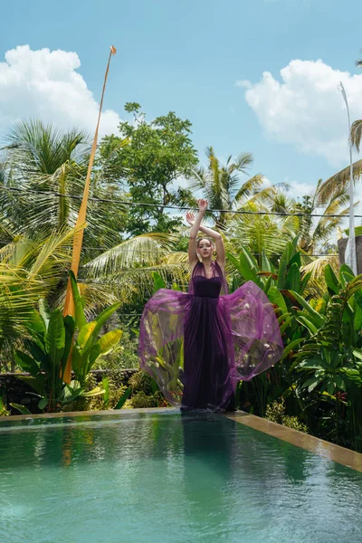 Aan de rand van het zwembad staat in een lange elegante jurk meisje foto gevouwen over het hoofd van haar handen Stockfoto