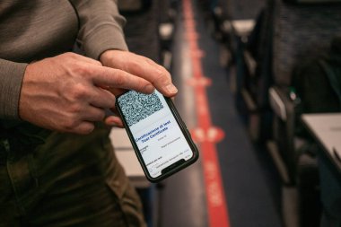 Bir adamın eli, Avrupa treninin kontrolü sırasında QR kodlu bir aşı sertifikası içeren bir telefon ekranını gösteriyor..
