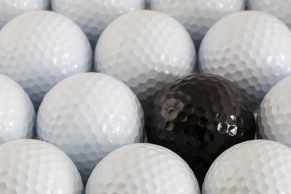 White golf balls and one black ball — Stock Photo, Image