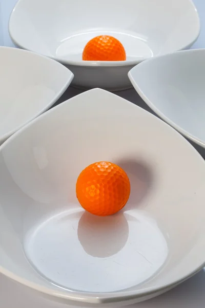 White ceramics bowls and orange golf ball — Stock Photo, Image