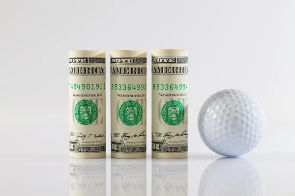 Rolos de notas de dólar e bola de golfe — Fotografia de Stock