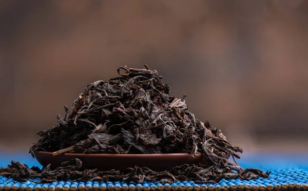 Primer plano de las hojas de té secas en un platillo de arcilla sobre una estera azul. —  Fotos de Stock