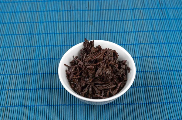 Hojas de té después de la preparación en un tazón blanco en una estera azul. —  Fotos de Stock