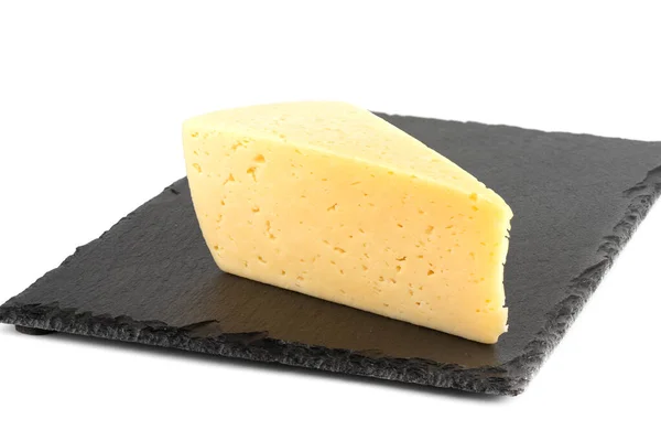Un trozo de queso en una tabla de cortar piedra sobre un fondo blanco. — Foto de Stock