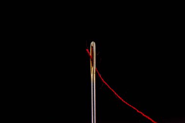 Siyah arka planda izole edilmiş bir iğnenin gözündeki kırmızı iplik..