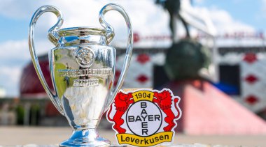 14 Haziran 2021, Leverkusen, Almanya. Bayer 04 Leverkusen futbol kulübü ve UEFA Şampiyonlar Ligi Kupası 'nın amblemi modern bir stadyumun arka planına karşıdır..